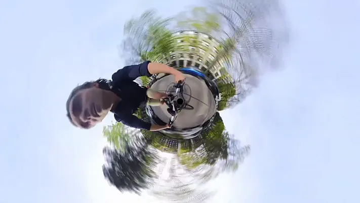 360 video 1 360-degree shot in little-planet style: person holding a camera pole between trees and buildings.