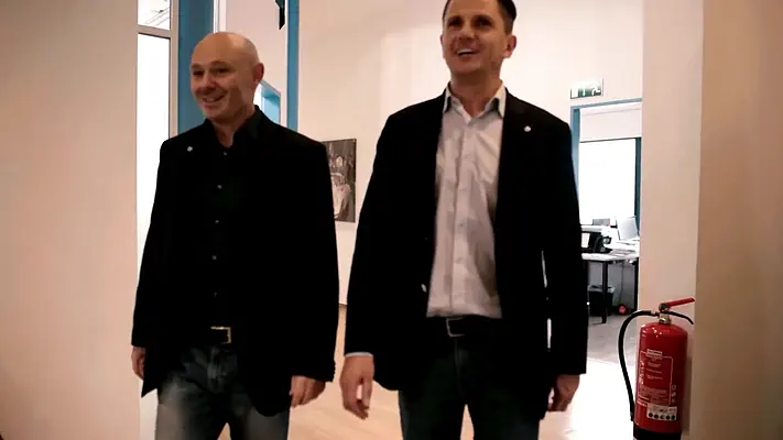 Bewerbungsvideo 2 Zwei Männer in Sakkos gehen lächelnd durch ein helles Büro.
