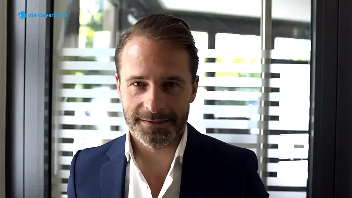 EB-Video Team 1 Portrait of a businessman in a dark blazer in front of an office glass door.