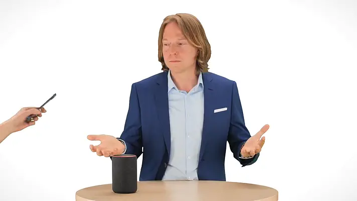 Blue / Green Screen 11 Mann im Anzug gestikuliert an einem Tisch mit Smart Speaker in einem weißen virtuellen Set.